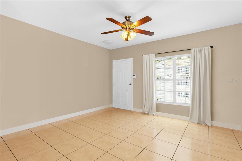 An empty room with beige walls, tan tile flooring, a ceiling fan, and white curtains — 727 SHROPSHIRE LOOP, SANFORD, FL