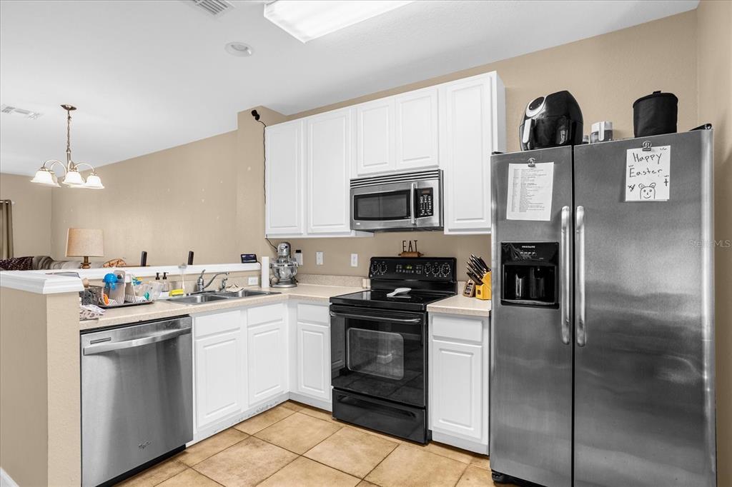A kitchen features white cabinets, stainless steel appliances, and tan tile flooring — 727 SHROPSHIRE LOOP, SANFORD, FL