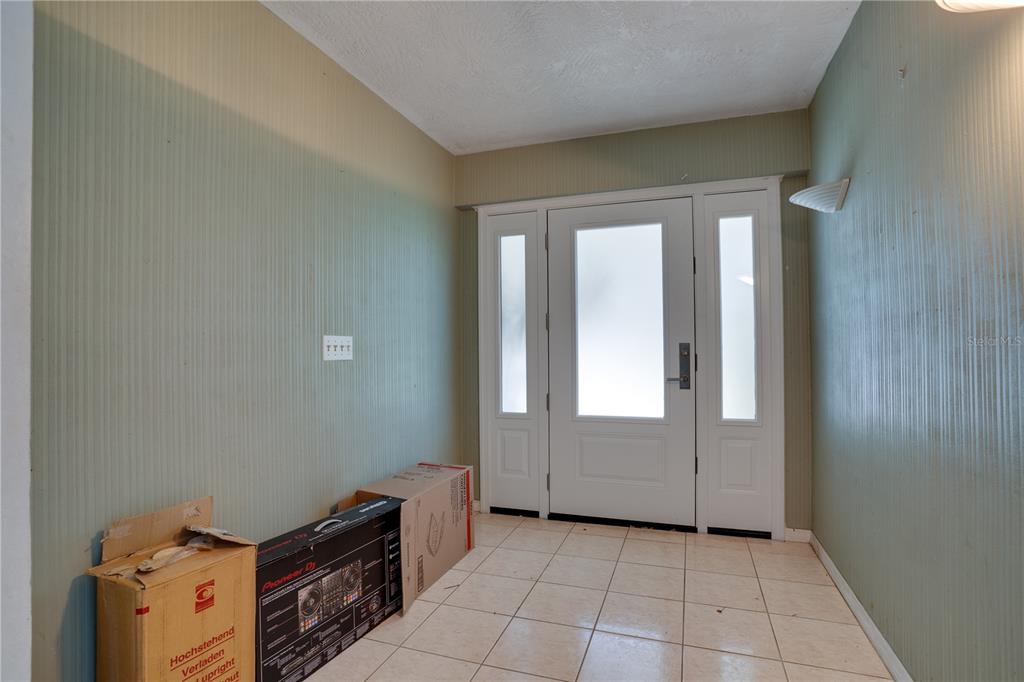 An entryway features light green vertical-striped wallpaper, white tile flooring, and a white front door — 11051 130TH AVENUE, LARGO, FL