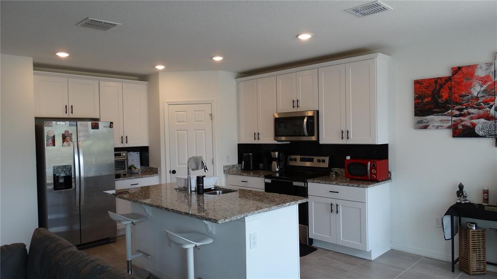 A kitchen features white cabinets, granite countertops, a center island with stools, and stainless appliances — 3138 VICEROY COURT, KISSIMMEE, FL