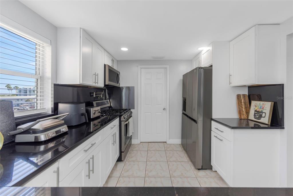 A kitchen features white cabinets, black countertops, stainless steel appliances, and light tile flooring — 1819 SHORE DRIVE S UNIT 318, SOUTH PASADENA, FL