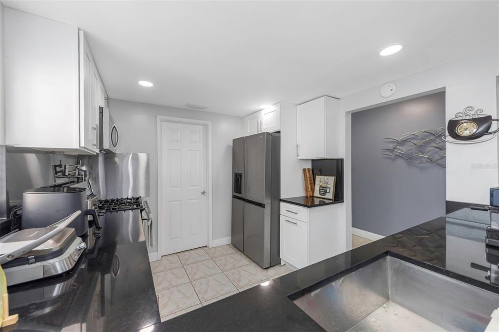 A kitchen features white cabinets, black countertops, stainless steel appliances, and light-colored tile flooring — 1819 SHORE DRIVE S UNIT 318, SOUTH PASADENA, FL