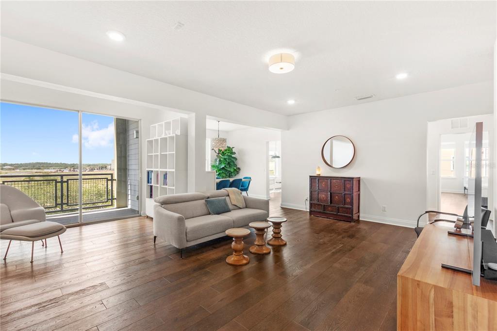 A living room with hardwood floors, a gray sofa, and a balcony with an outdoor view — 7573 LAUREATE BOULEVARD UNIT 1-307, ORLANDO, FL