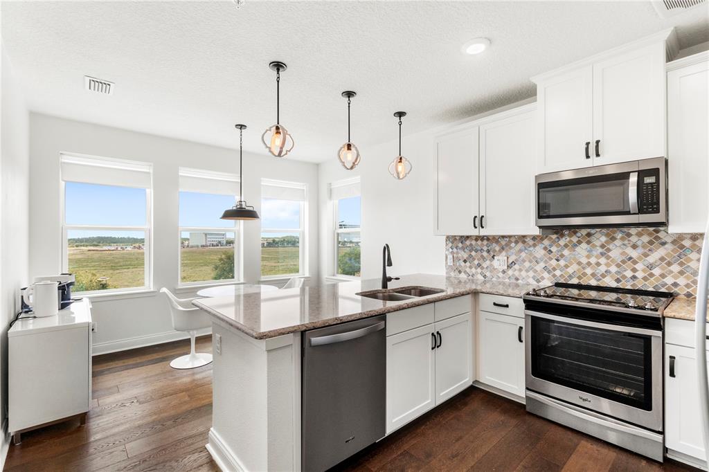 A modern kitchen features white cabinets, granite countertops, stainless steel appliances, and a tile backsplash — 7573 LAUREATE BOULEVARD UNIT 1-307, ORLANDO, FL