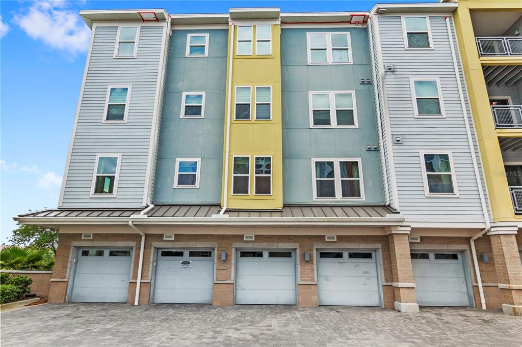 A multi-story apartment building exterior features five garage doors at street level — 7573 LAUREATE BOULEVARD UNIT 1-307, ORLANDO, FL