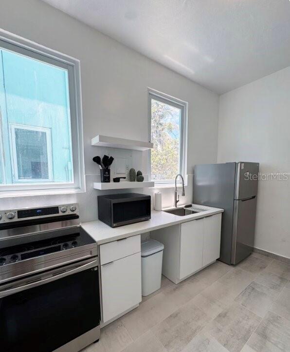 A modern kitchen features white cabinets, stainless steel appliances, and two windows — 250 CALLE DEL PARQUEZ UNIT 2B, SAN JUAN, PR