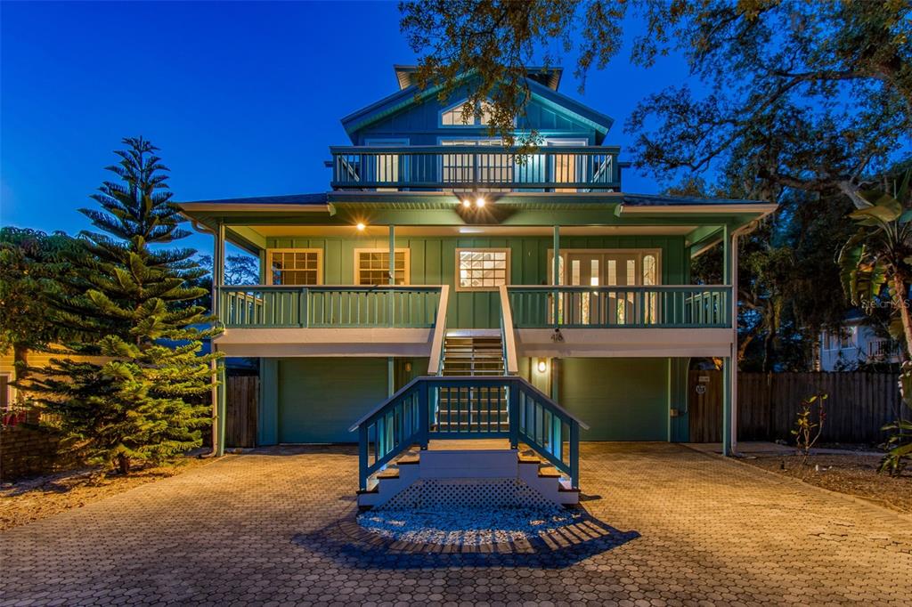 A three-story teal house with a raised porch, central staircase, and paved driveway at night — 416 TENNESSEE AVENUE, CRYSTAL BEACH, FL
