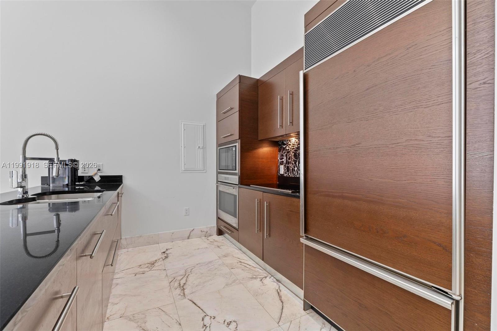 A modern kitchen features dark wood cabinetry, black countertops, and white marble flooring — 475 Brickell Ave # 2209, Miami FL 33131, MIAMI, FL