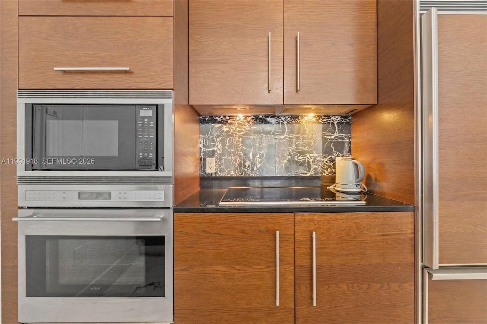A modern kitchen features wood-grain cabinetry, stainless steel appliances, and a black marble backsplash — 475 Brickell Ave # 2209, Miami FL 33131, MIAMI, FL
