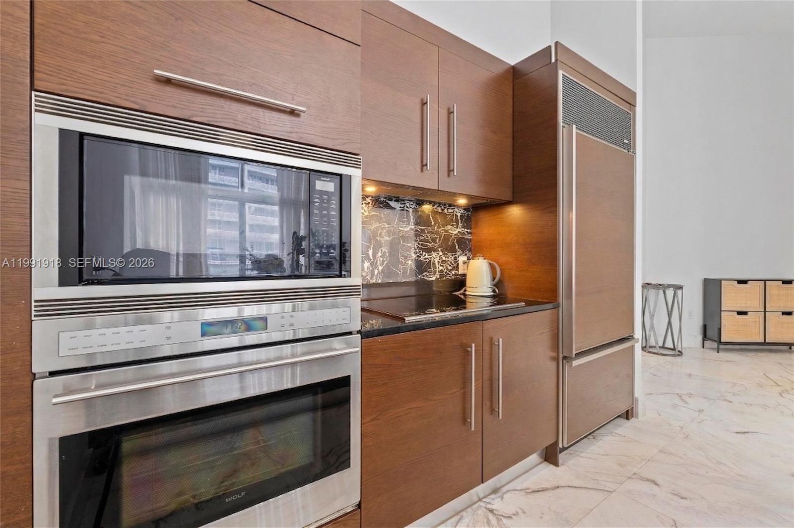 A modern kitchen features wood cabinetry, stainless steel appliances, and a black marble backsplash — 475 Brickell Ave # 2209, Miami FL 33131, MIAMI, FL