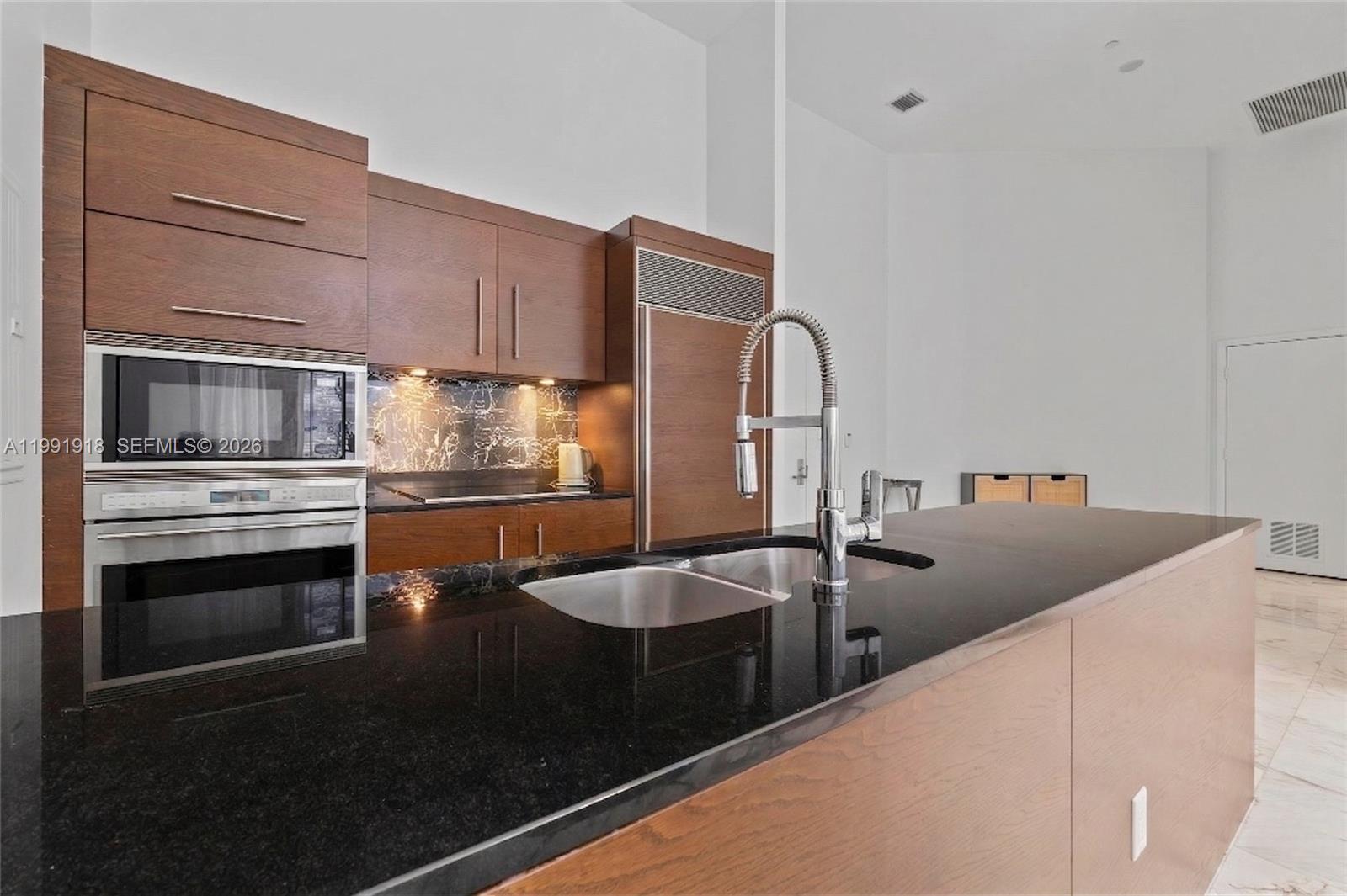 A modern kitchen features dark wood cabinetry, black granite countertops, and a stainless steel sink — 475 Brickell Ave # 2209, Miami FL 33131, MIAMI, FL