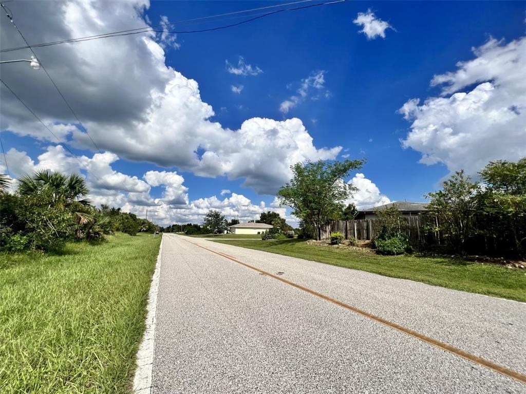 A paved road stretches toward a house under a bright blue sky with large clouds — 177 THERESA BOULEVARD, PORT CHARLOTTE, FL