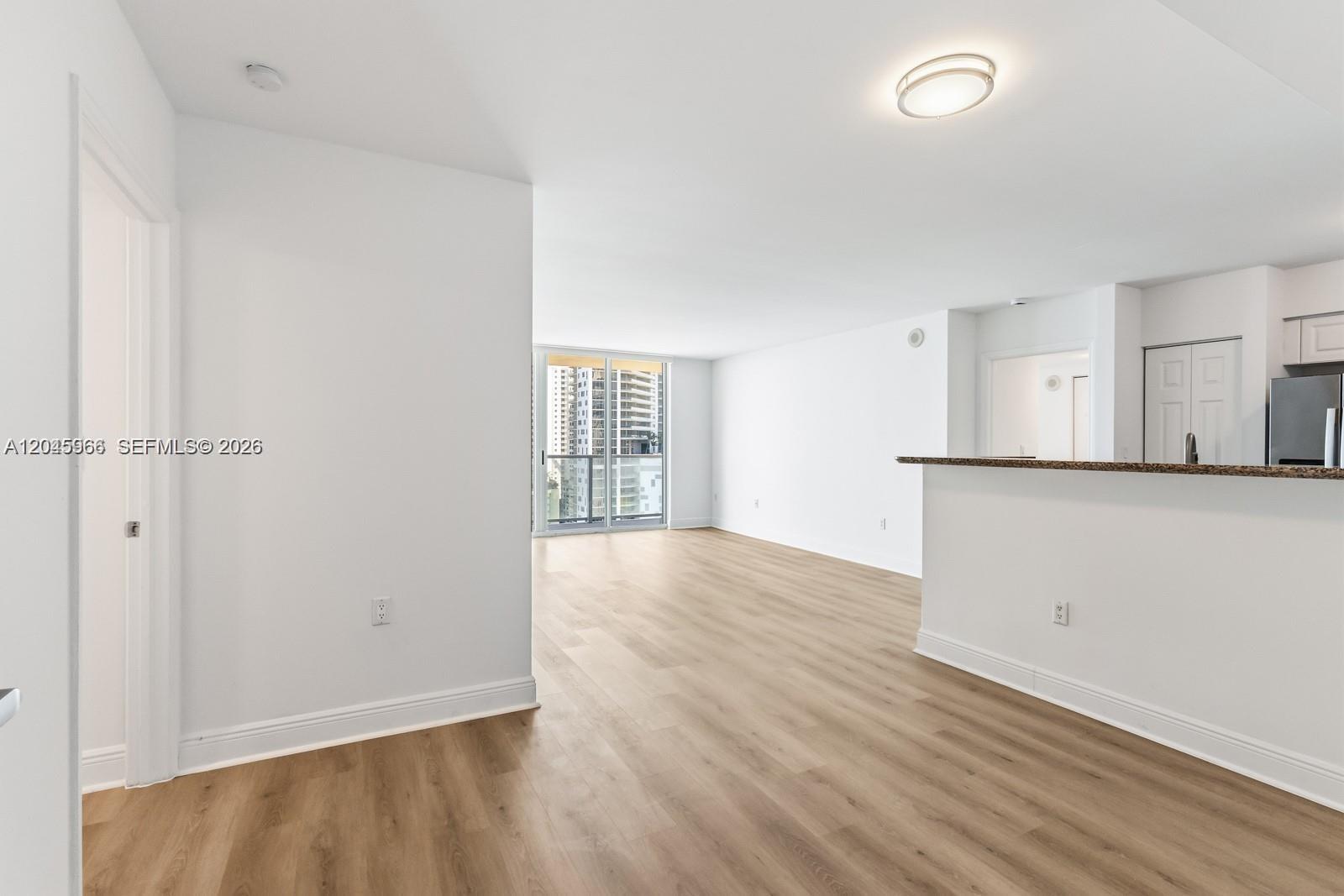 An open-concept living area features light wood-look flooring, white walls, and a kitchen breakfast bar — 1155 Brickell Bay Dr # 1609, Miami FL 33131, MIAMI, FL
