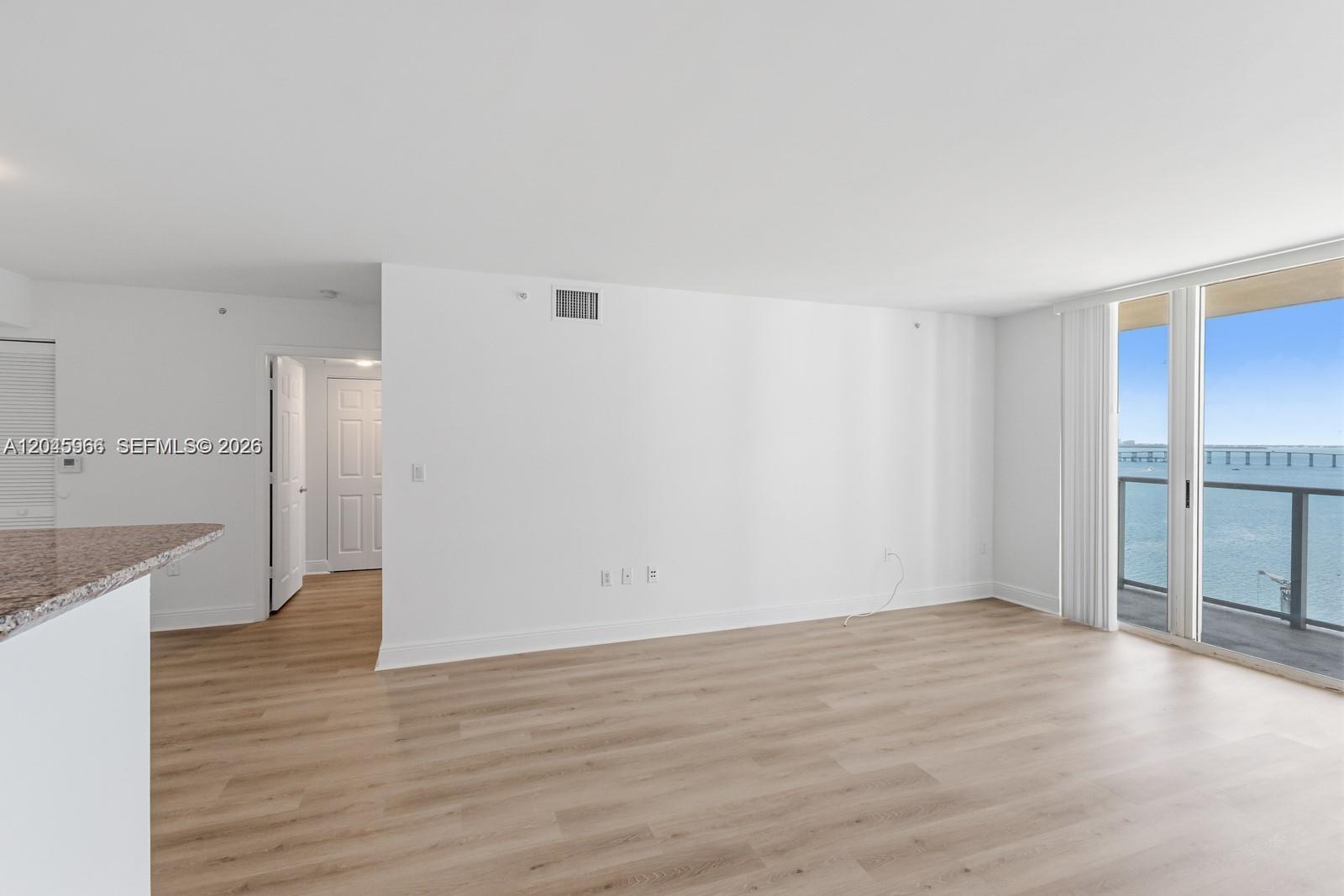 An empty living area features light wood-look flooring, white walls, and a balcony overlooking water — 1155 Brickell Bay Dr # 1609, Miami FL 33131, MIAMI, FL
