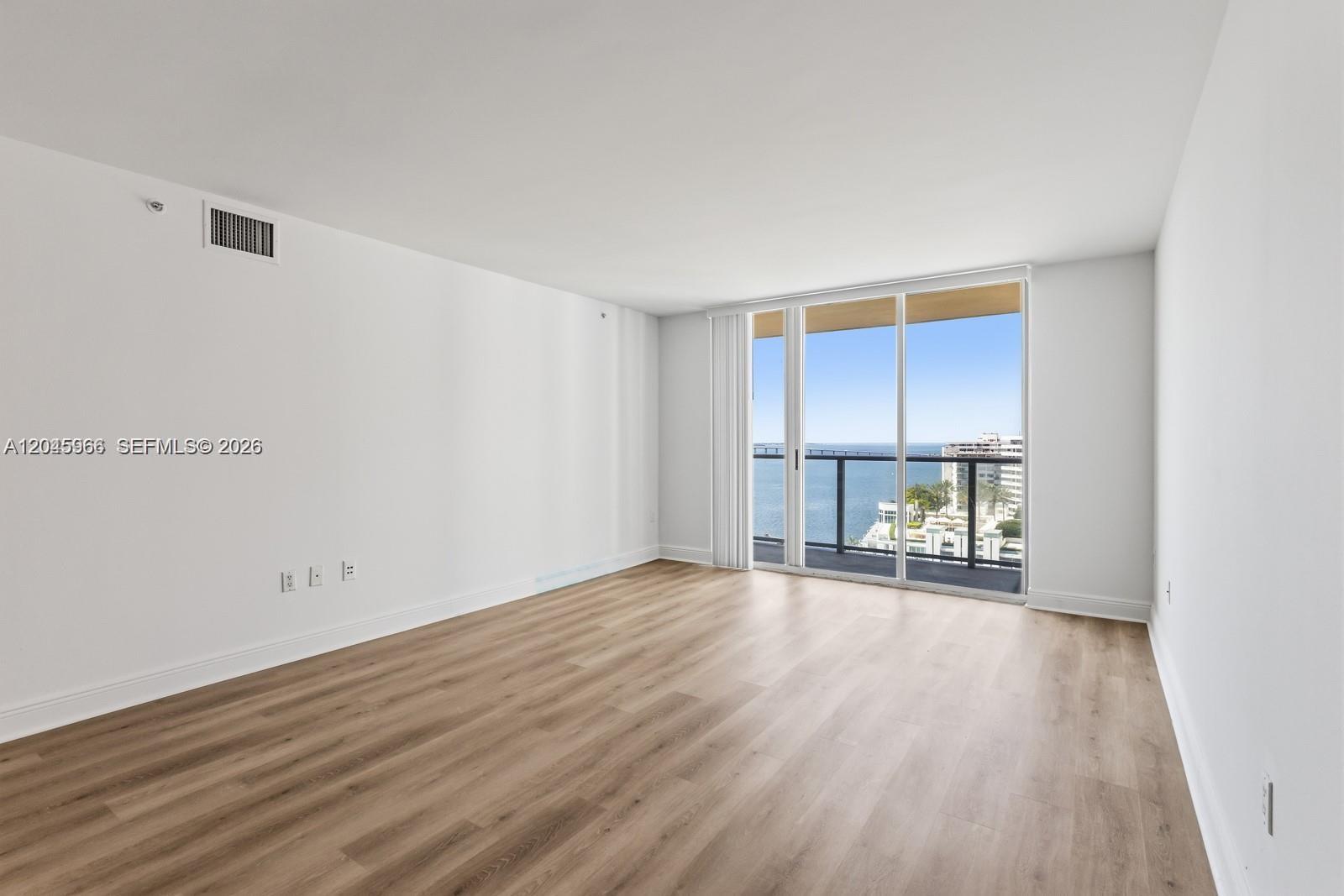 An empty room with light wood-look flooring and a sliding glass door overlooking the ocean — 1155 Brickell Bay Dr # 1609, Miami FL 33131, MIAMI, FL