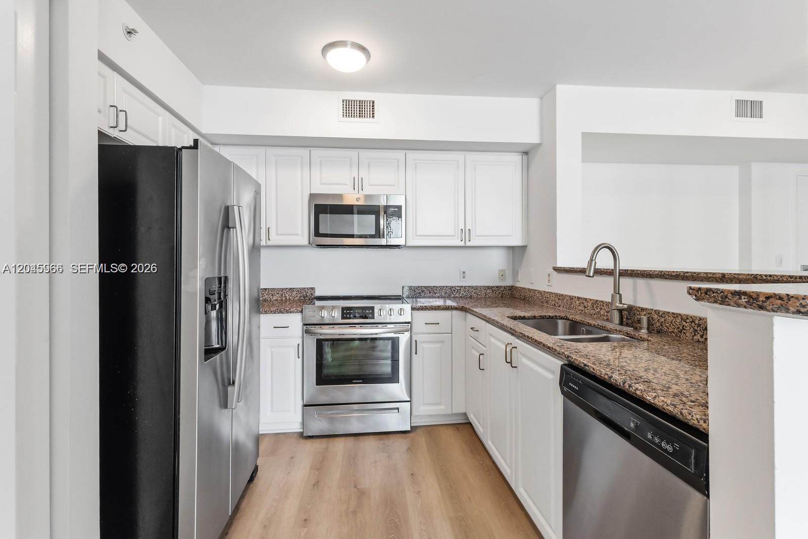 A kitchen features white cabinets, granite countertops, and stainless steel appliances on wood-look flooring — 1155 Brickell Bay Dr # 1609, Miami FL 33131, MIAMI, FL