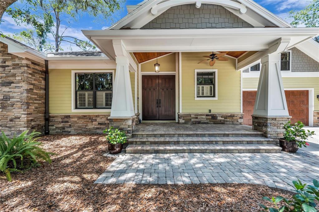 A front exterior view of a house featuring a stone facade, porch, and double doors — 5911 RIVER FOREST CIRCLE, BRADENTON, FL