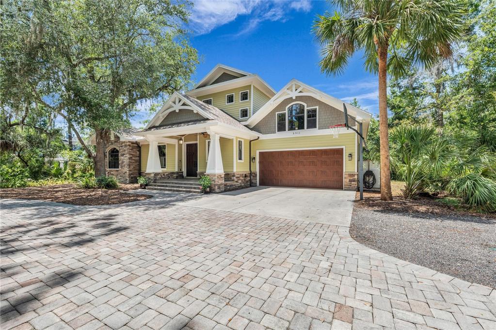 A two-story house with light green siding, stone accents, a paved driveway, and a basketball hoop — 5911 RIVER FOREST CIRCLE, BRADENTON, FL