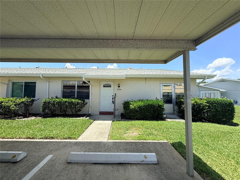 A single-story residential unit with a white door, concrete walkway, and a covered parking area — 2304 GLENMORE CIRCLE UNIT 327, SUN CITY CENTER, FL