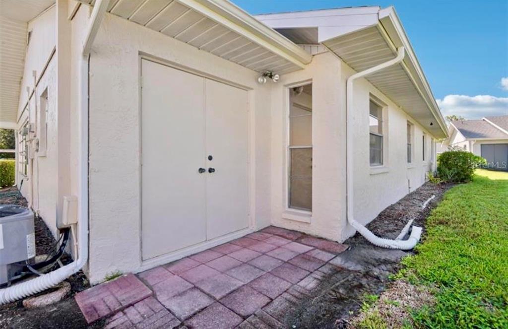 A paved patio area features a double-door storage closet and a white downspout — 2304 GLENMORE CIRCLE UNIT 327, SUN CITY CENTER, FL