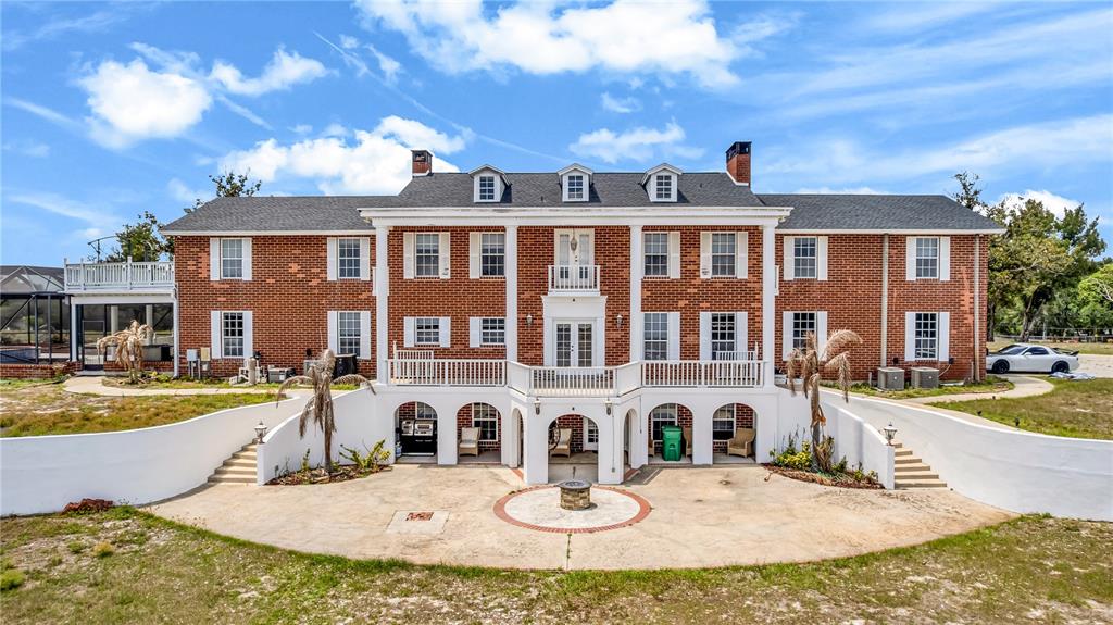 A large two-story brick house features a white balcony, arched lower-level openings, and a patio — 1585 S CARPENTER ROAD, TITUSVILLE, FL