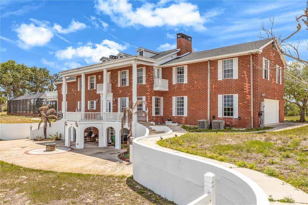 A large two-story red brick house features a white columned porch and a lower-level patio — 1585 S CARPENTER ROAD, TITUSVILLE, FL