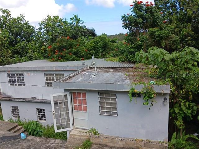 A two-story gray concrete house with a flat roof and louvered windows sits on a hill — 115 COM SANTA CATALINA 228 UNIT 228, CANOVANAS, PR