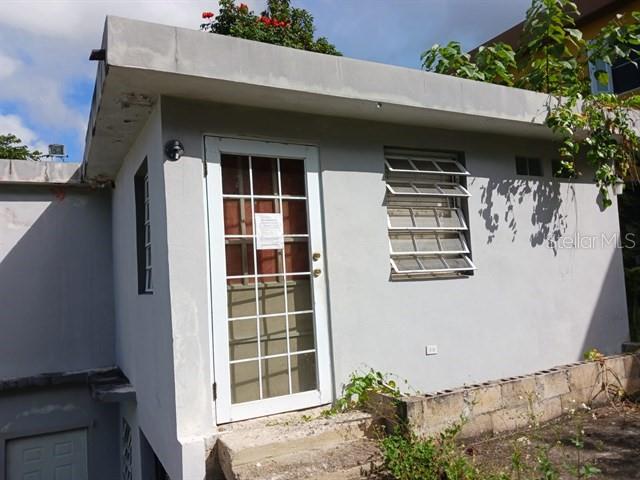 A single-story gray concrete structure features a white-framed glass door and a louvered window — 115 COM SANTA CATALINA 228 UNIT 228, CANOVANAS, PR