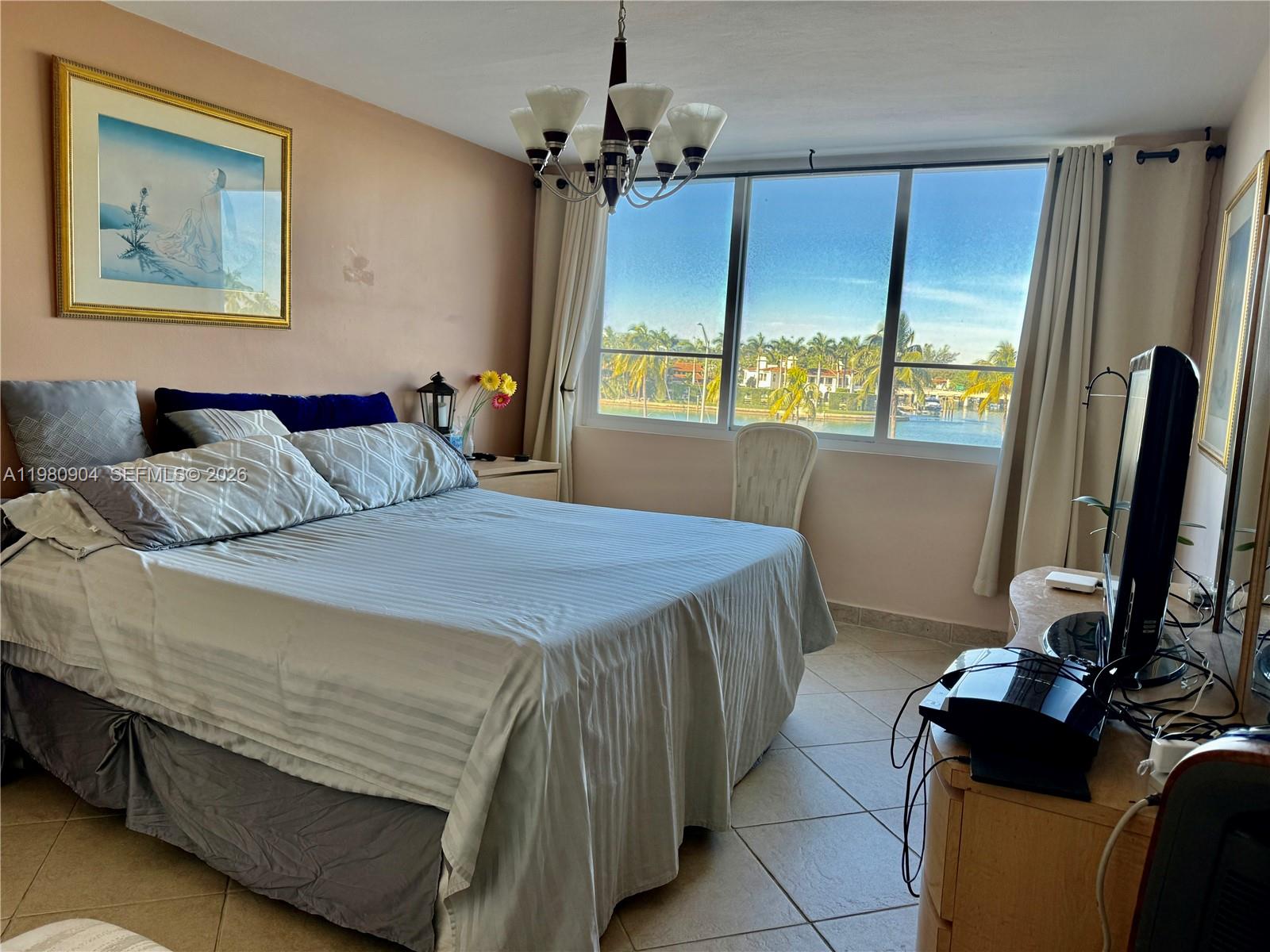 A bedroom features a bed, a television, and a large window overlooking a waterfront view — 5005 Collins Ave # 304, Miami Beach FL 33140, MIAMI BEACH, FL