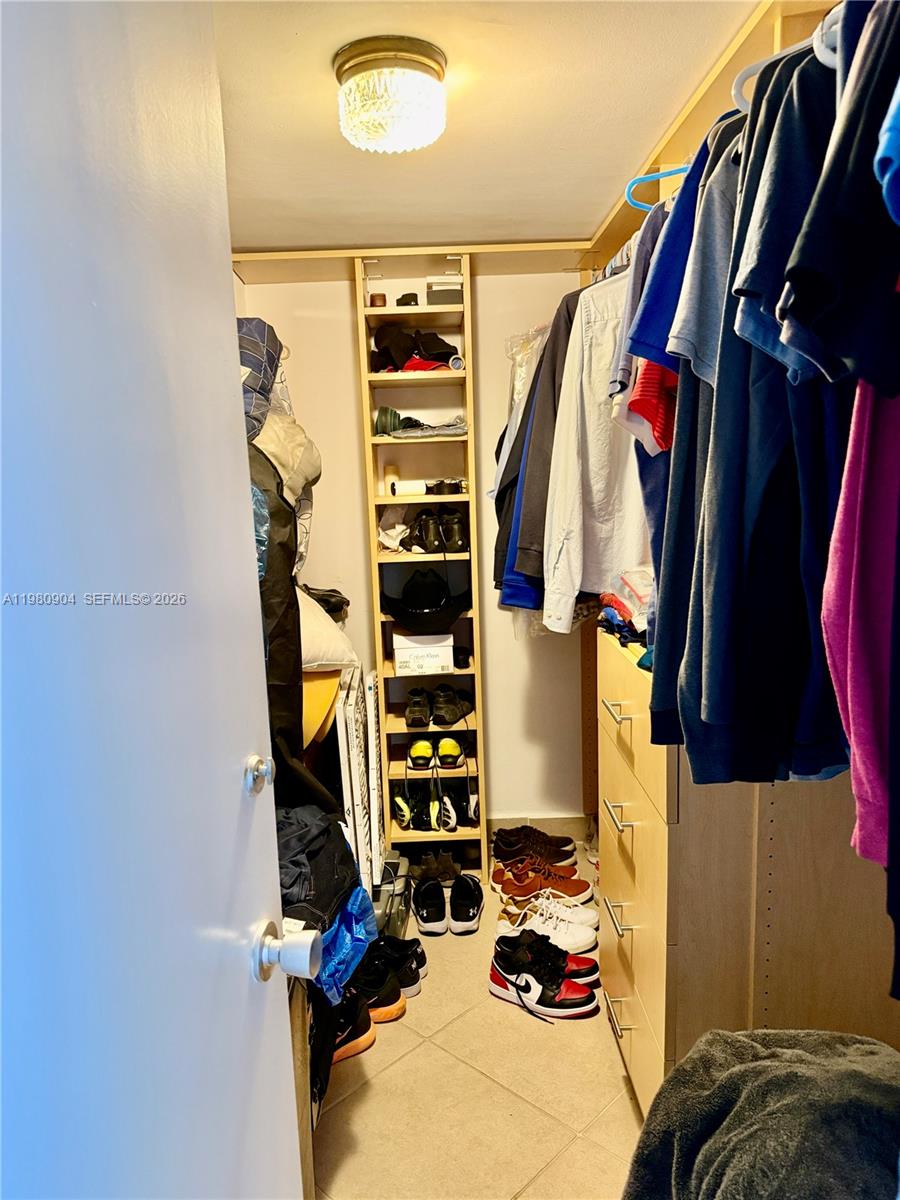 A walk-in closet features hanging clothes, a central shelving unit, and shoes on the floor — 5005 Collins Ave # 304, Miami Beach FL 33140, MIAMI BEACH, FL