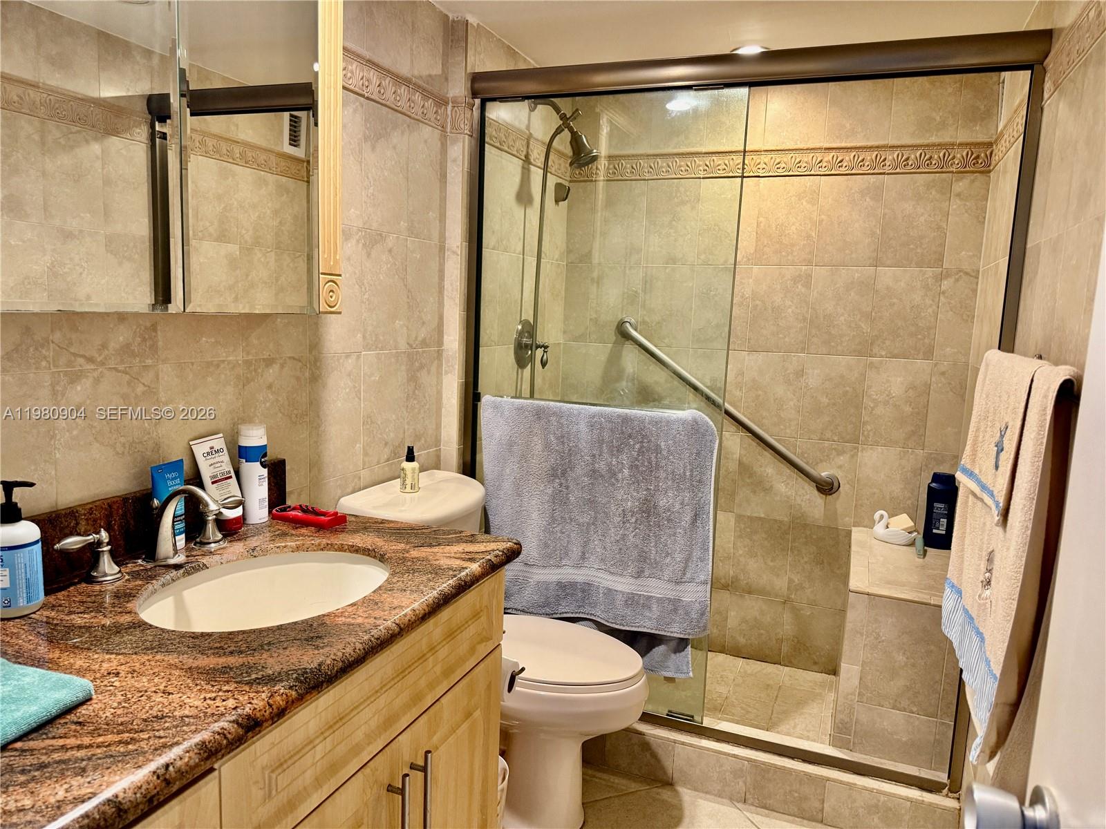 A bathroom features a granite vanity, a toilet, and a tiled walk-in shower with glass doors — 5005 Collins Ave # 304, Miami Beach FL 33140, MIAMI BEACH, FL