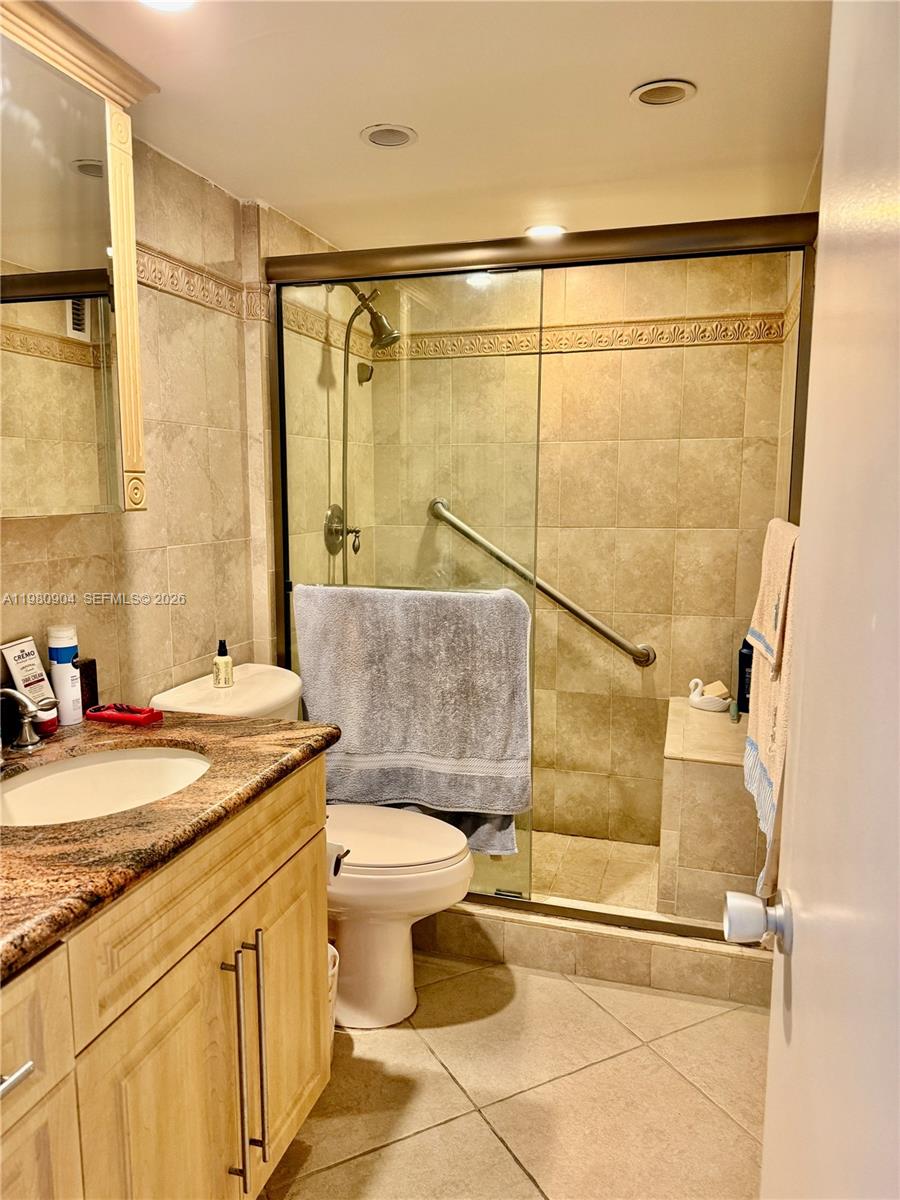 A bathroom features a granite-topped vanity, a toilet, and a tiled walk-in shower with glass doors — 5005 Collins Ave # 304, Miami Beach FL 33140, MIAMI BEACH, FL