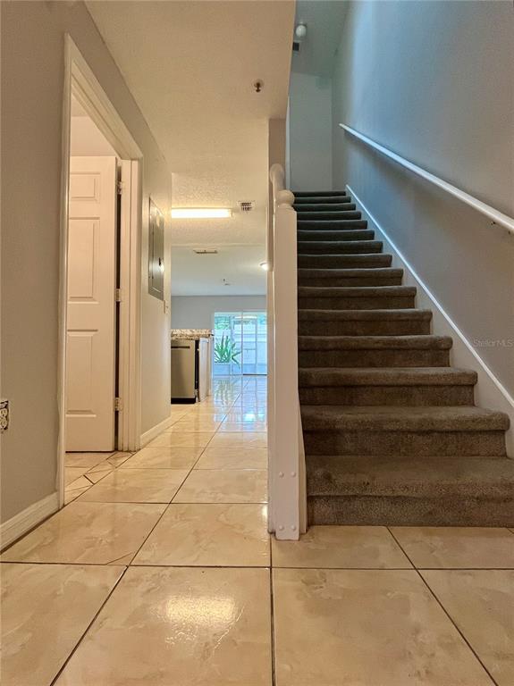 A hallway with tiled floors leads to a kitchen, with a carpeted staircase on the right — 1647 WINDSOR OAK COURT, KISSIMMEE, FL