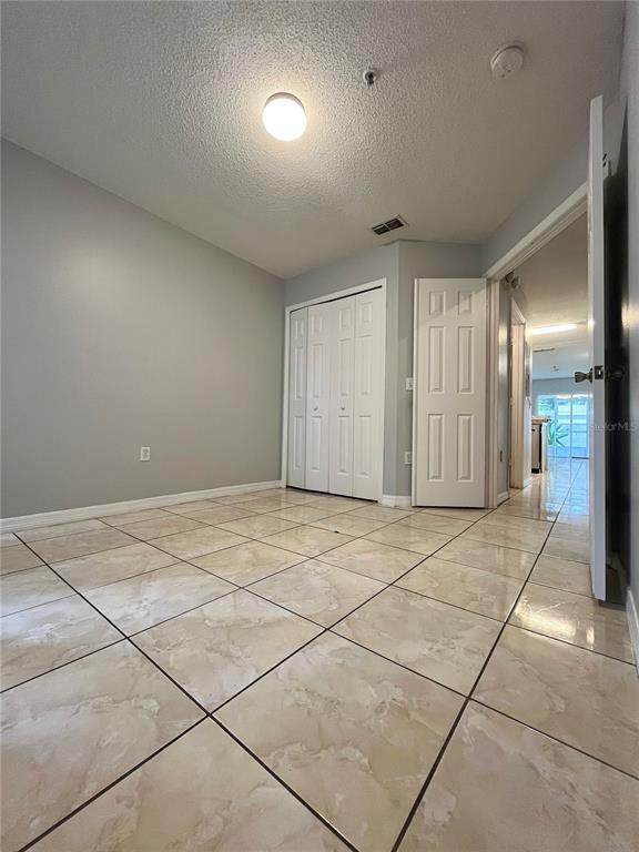 A room with light gray walls, white closet doors, and beige tile flooring — 1647 WINDSOR OAK COURT, KISSIMMEE, FL