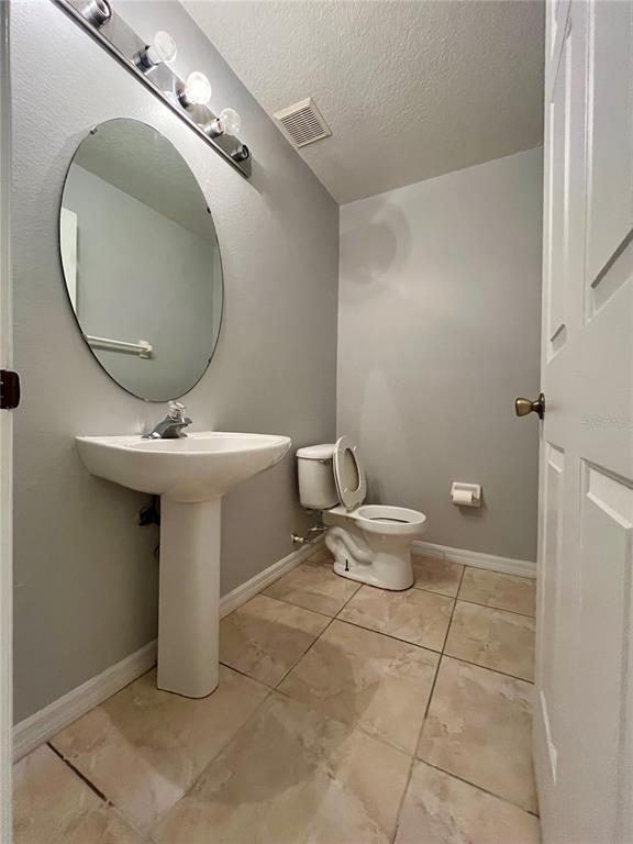 A half bathroom features a pedestal sink, oval mirror, toilet, and light-colored tile flooring — 1647 WINDSOR OAK COURT, KISSIMMEE, FL
