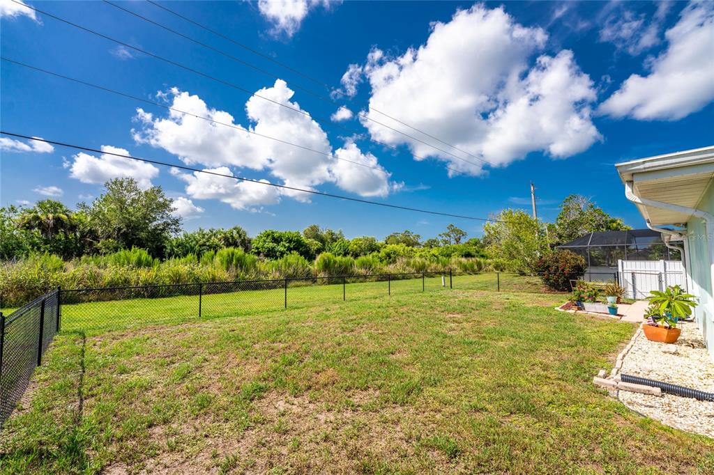 A grassy backyard features a chain-link fence, a patio area, and a view of trees — 23 ANNAPOLIS LANE, ROTONDA WEST, FL