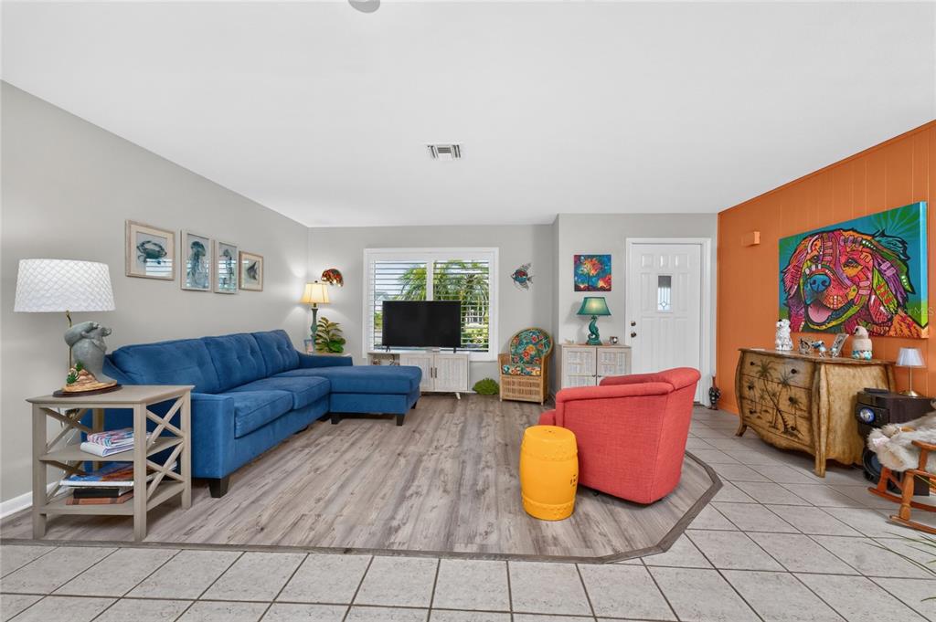 A living room features a blue sectional sofa, a red armchair, and wood-look flooring — 23 ANNAPOLIS LANE, ROTONDA WEST, FL