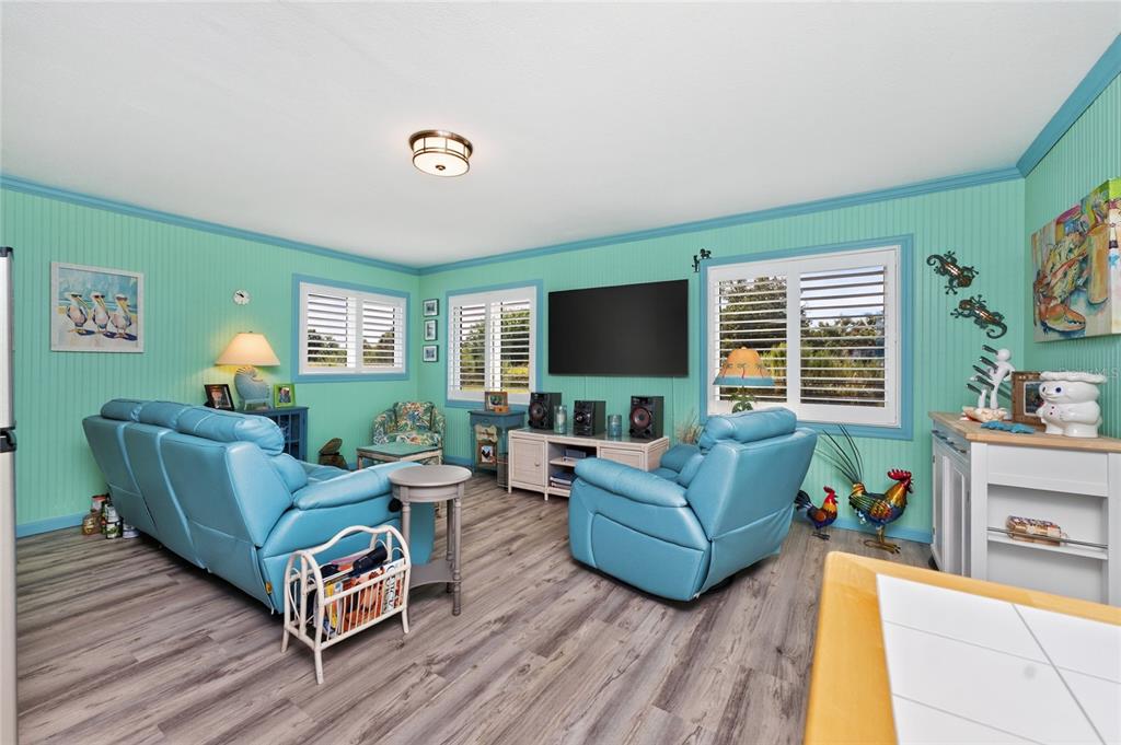 A living room with turquoise beadboard walls, blue leather furniture, and wood-look flooring — 23 ANNAPOLIS LANE, ROTONDA WEST, FL