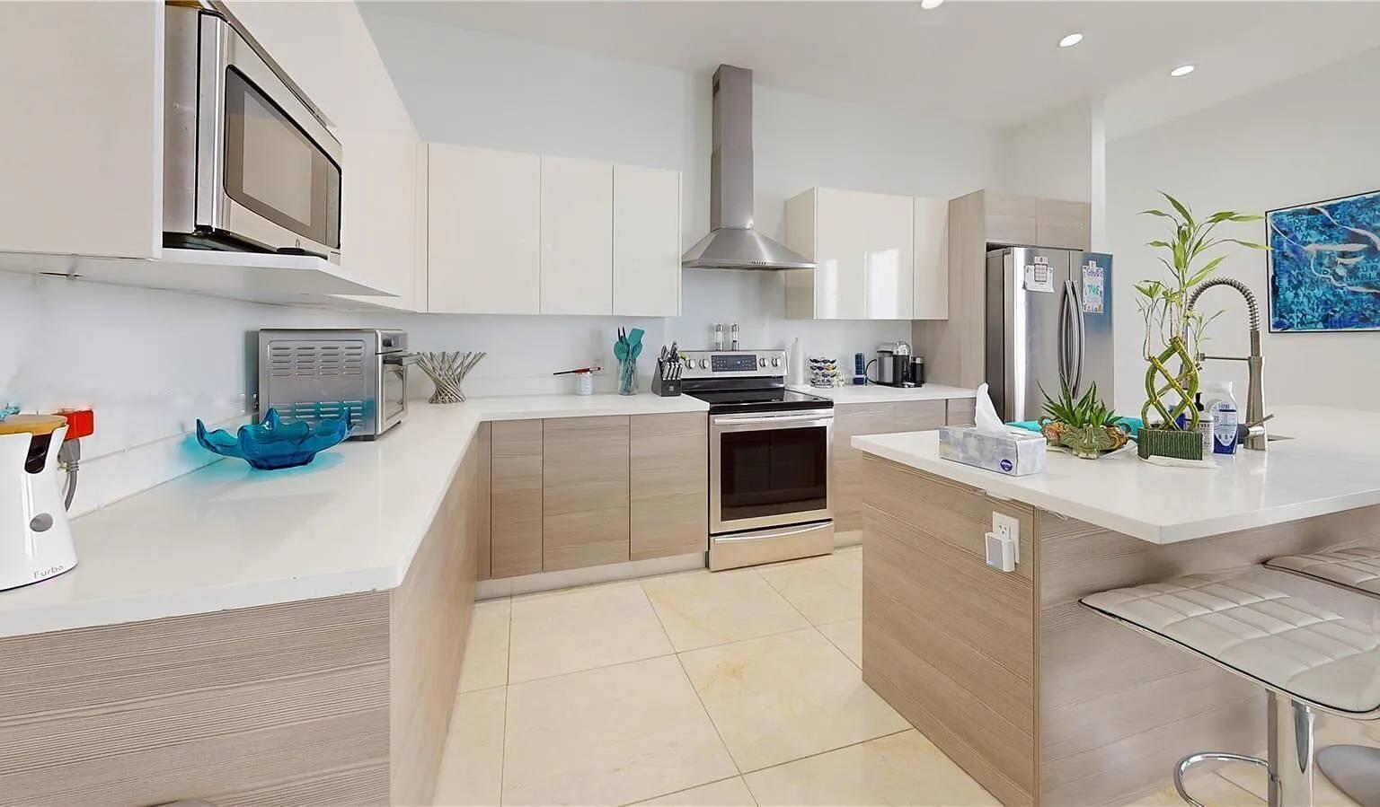 A modern kitchen features white upper cabinets, light wood lower cabinets, and a central island — 3091 SW 21st Street, Miami FL 33145, MIAMI, FL