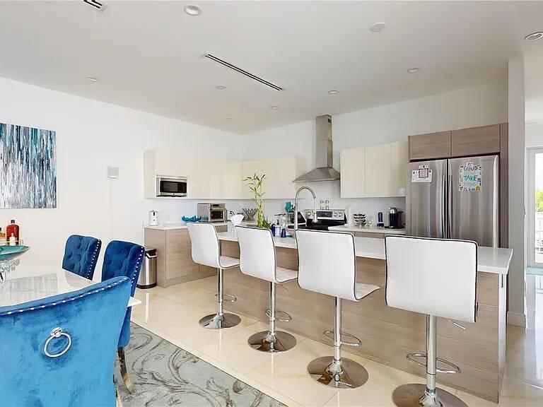 A modern kitchen features a breakfast bar with four white stools and stainless steel appliances — 3091 SW 21st Street, Miami FL 33145, MIAMI, FL