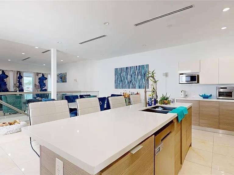 A modern kitchen features a large white island, light wood cabinetry, and a dining area — 3091 SW 21st Street, Miami FL 33145, MIAMI, FL