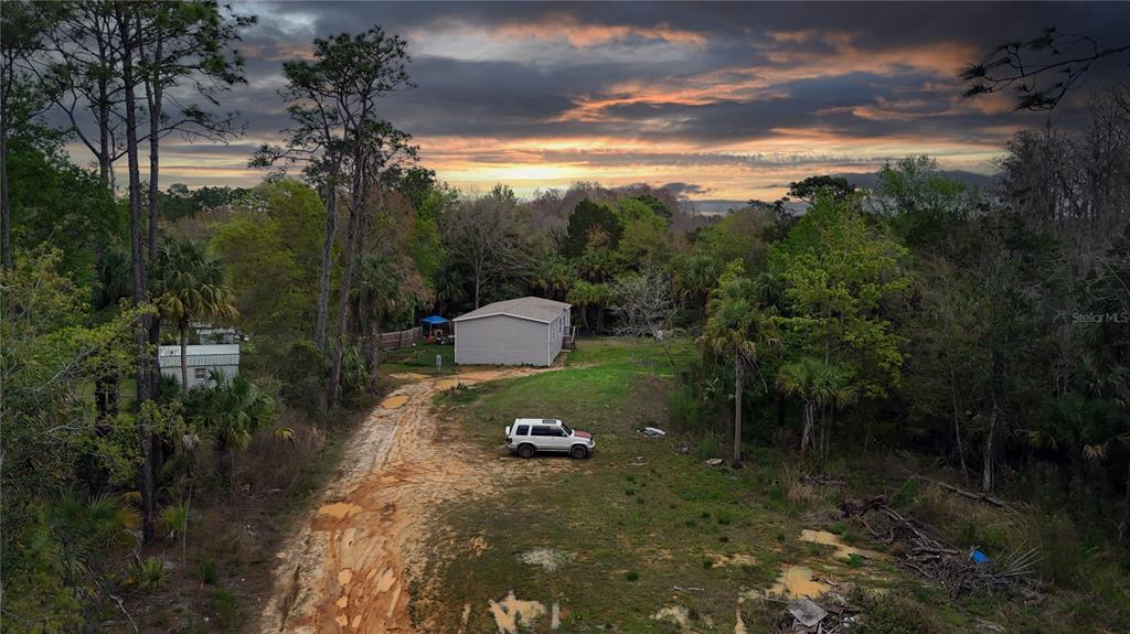 An aerial view shows a house and a vehicle on a dirt road amidst trees — 7697 W RADIANCE LANE, HOMOSASSA, FL