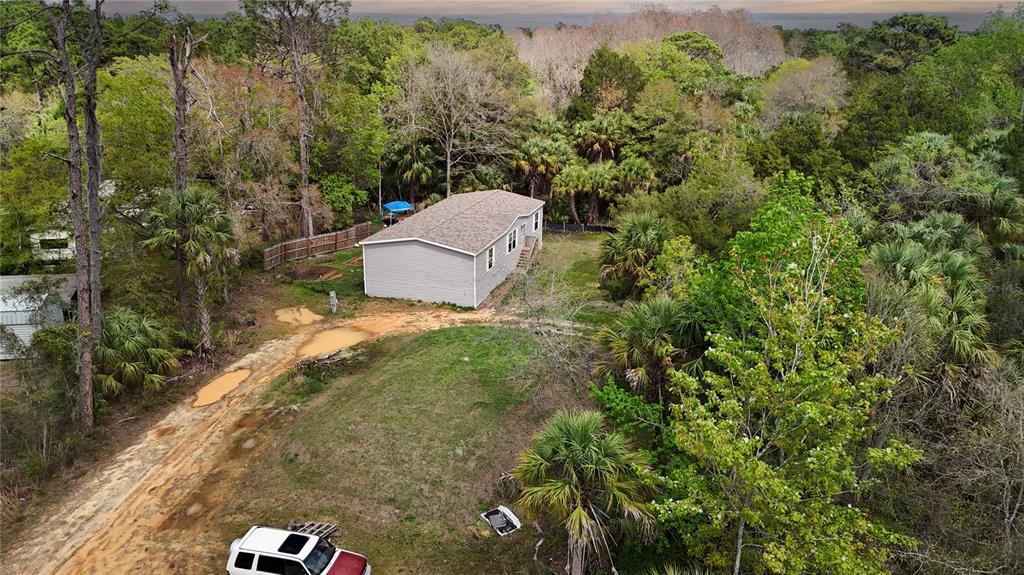 An aerial view shows a light-colored house surrounded by dense trees and a dirt driveway — 7697 W RADIANCE LANE, HOMOSASSA, FL