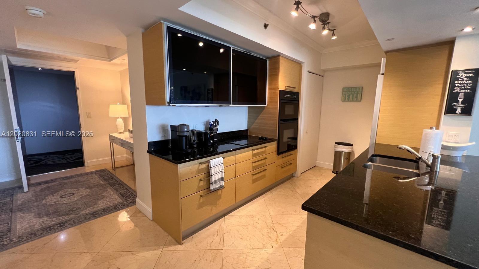 A modern kitchen features light wood cabinets, black countertops, and a built-in wall oven — 1830 S Ocean Dr # 2204, Hallandale Beach FL 33009, HALLANDALE BEACH, FL