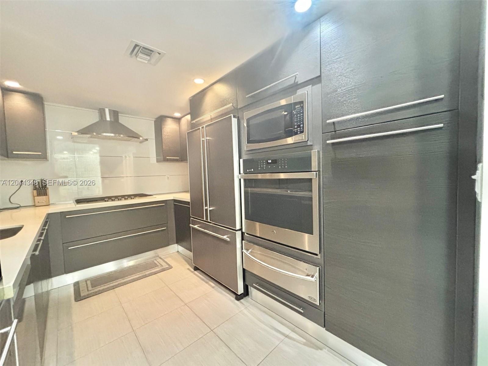 A modern kitchen features dark gray cabinetry, stainless steel appliances, and light-colored tile flooring — 2030 S Ocean Dr # 423, Hallandale Beach FL 33009, HALLANDALE BEACH, FL