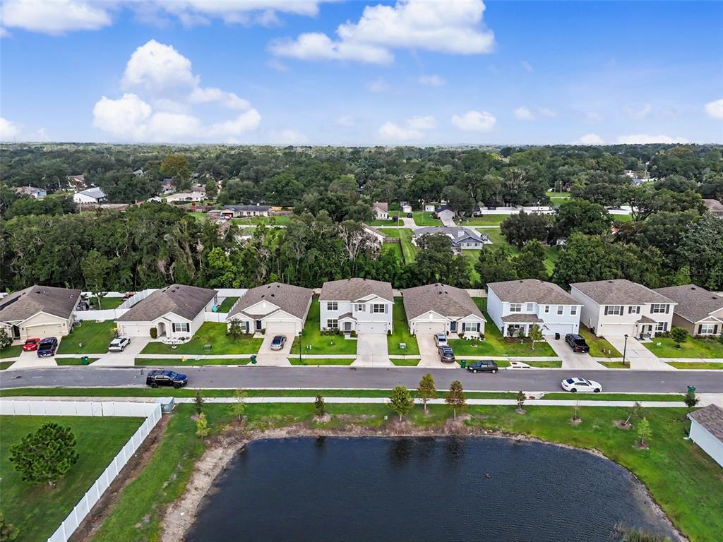 An aerial view shows a row of suburban houses facing a pond and street — 36851 GOFFAUX LOOP, ZEPHYRHILLS, FL
