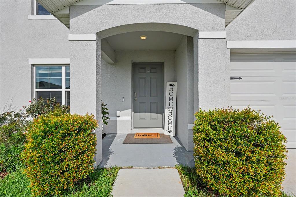 The exterior of a house features a gray front door, a porch, and two bushes — 36851 GOFFAUX LOOP, ZEPHYRHILLS, FL