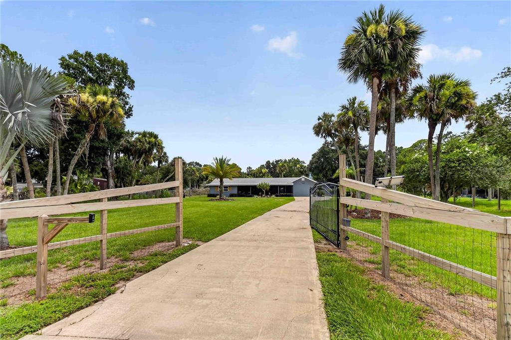 A concrete driveway leads through a gated wooden fence toward a single-story house — 4105 RECTOR ROAD, COCOA, FL