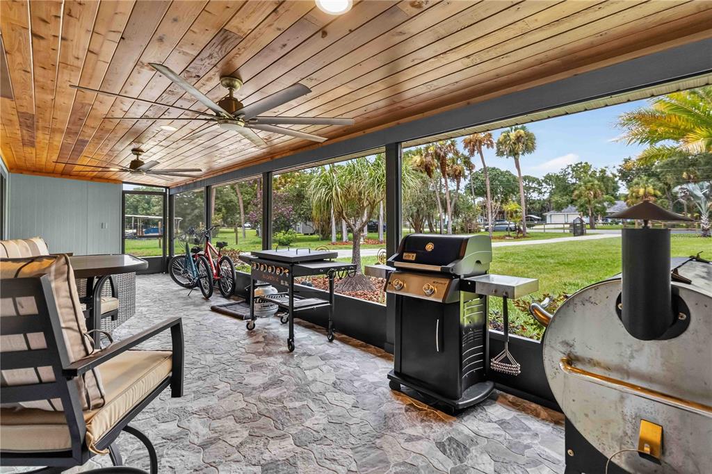A screened-in porch features a wood-plank ceiling, stone-patterned flooring, and multiple outdoor grills — 4105 RECTOR ROAD, COCOA, FL