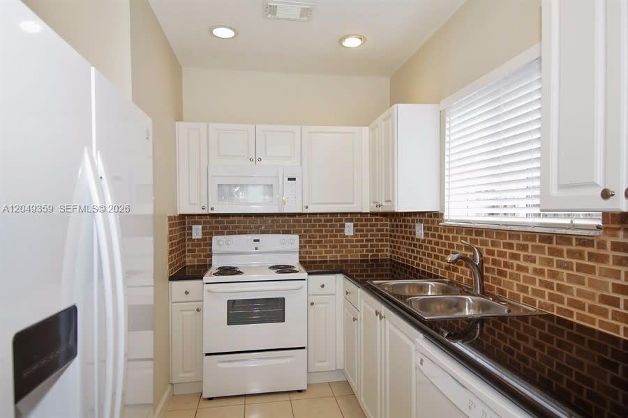 A kitchen features white cabinets, a white stove, a double sink, and brown brick backsplash — HOMESTEAD, FL